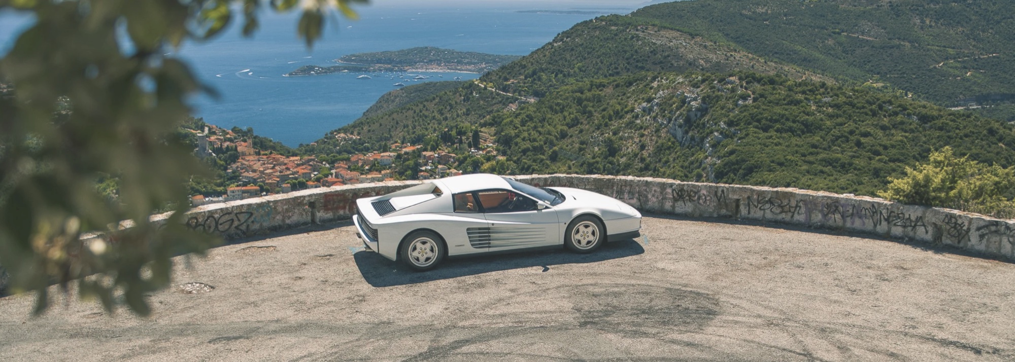 A Ferrari Testarossa on a coastal road above the Mediterranean